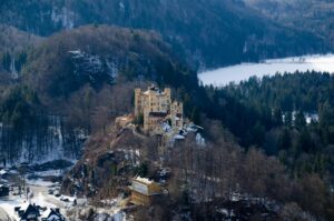 Füssen bavaria Aerial view of a historic castle surrounded by snowy forests and mountains in winter light.